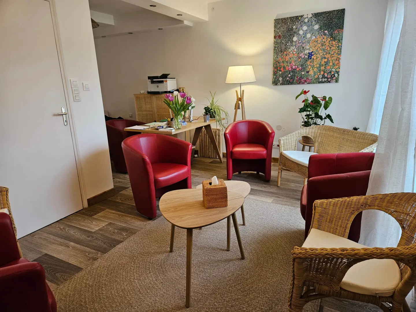 Le cabinet : fauteuils rouges autour d'une table basse en bois, deux fauteuils en osier, un tableau de fleurs au mur