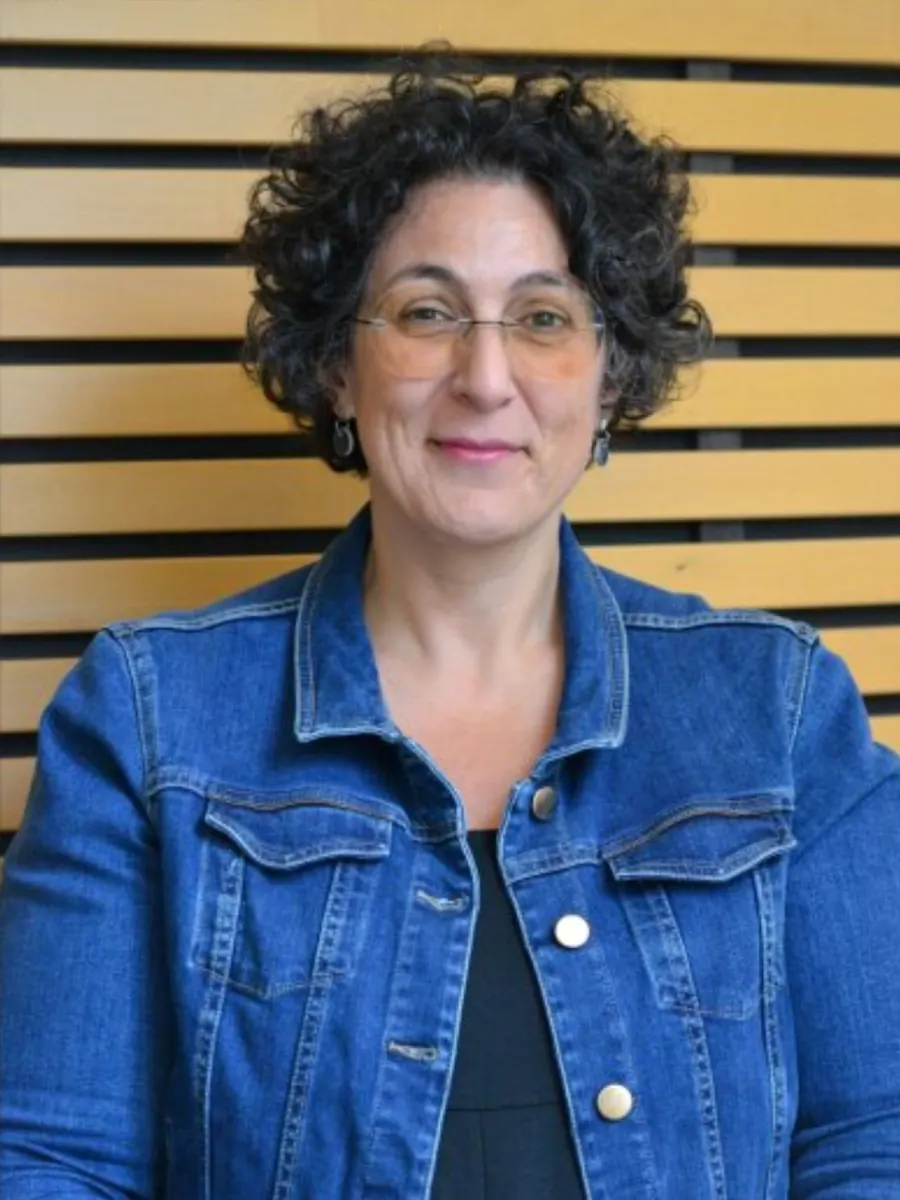 Portrait du Dr Antonella D'Annunzio, en veste en jean devant un mur à lattes de bois